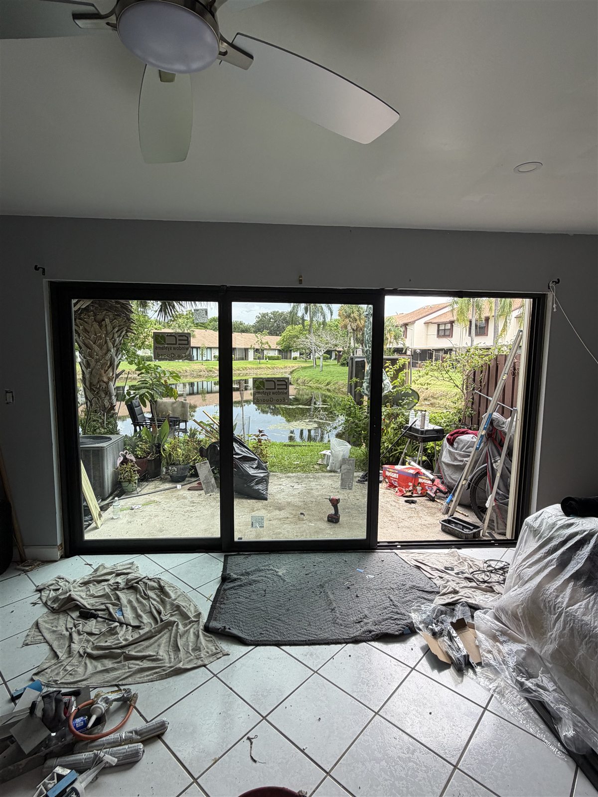 The same opening after installation, fitted with a dark bronze three-panel Eco-Guard impact sliding glass door looking out across the lake