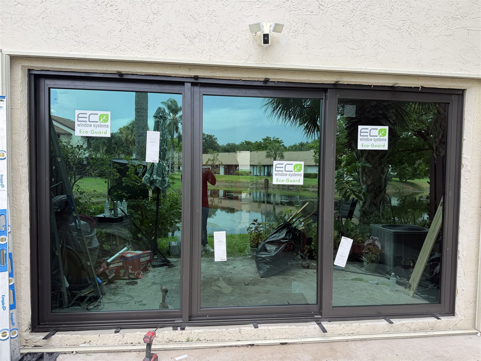 Eco Window Systems Eco-Guard three-panel impact sliding glass door installed in a Coconut Creek townhouse, manufacturer labels still on the glass, looking out across the lake