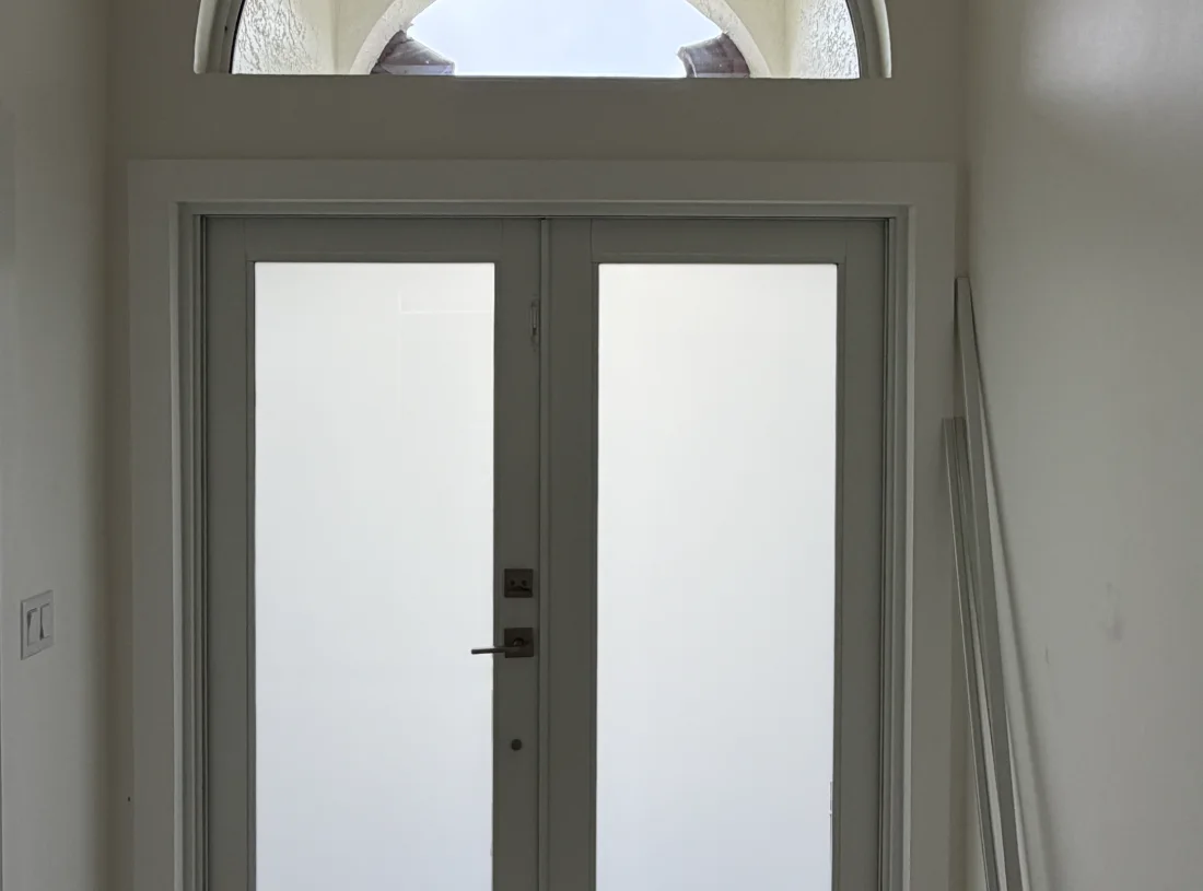 Double impact entry doors with frosted glass panels and an arched transom, seen from inside the entrance hall