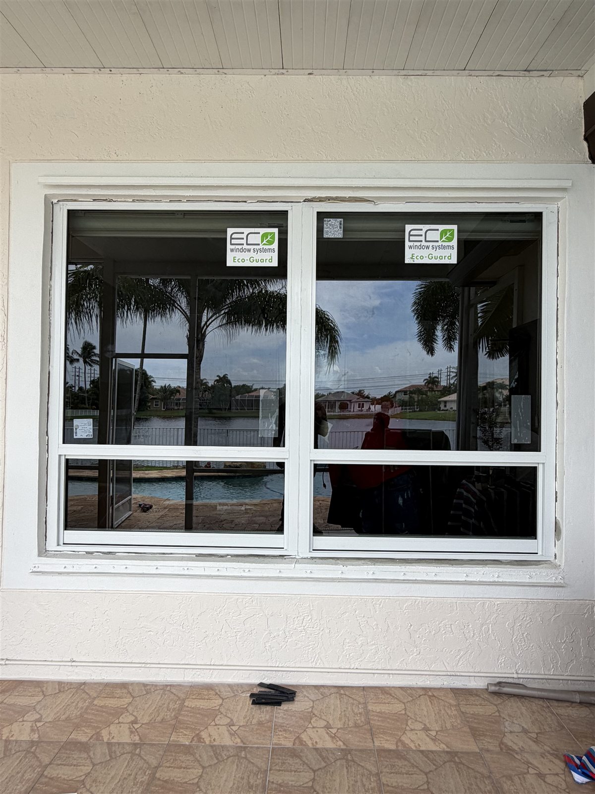 The same patio opening after installation, fitted with two white-framed Eco-Guard impact windows looking out over the pool and lake