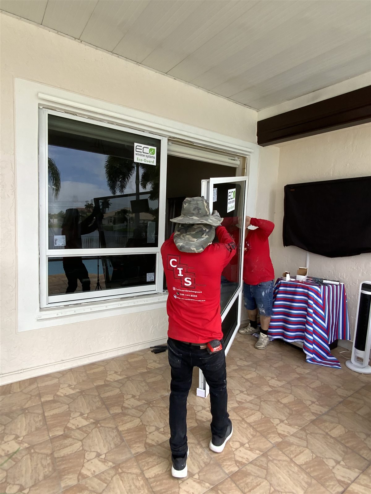 Two ClearView installers setting a white-framed Eco-Guard impact window into a patio opening during a whole-house replacement in Pembroke Pines